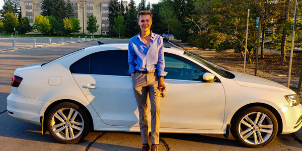 Portrait of young man standing by car