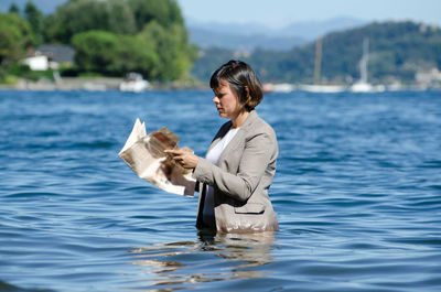 Side view of woman reading newspaper while standing in lake