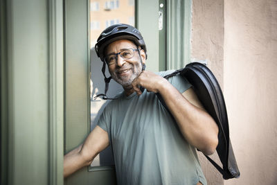 Smiling senior man with bag by doorway outside house