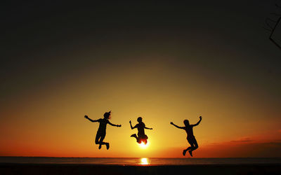 Silhouette people jumping on beach against clear sky during sunset