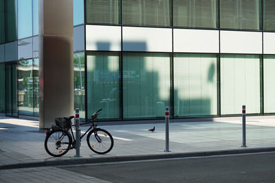 Bicycle parked by bollard on footpath against office building