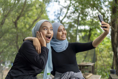 Young woman taking selfie with friend outdoors