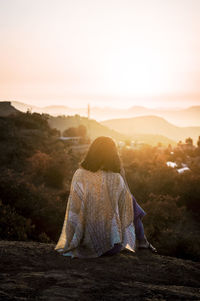 Rear view of woman looking at mountains against sky during sunset