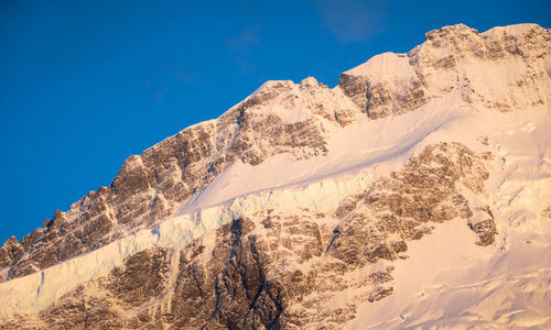 Low angle view of snowcapped mountains against clear blue sky