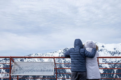 Men standing by railing against sky during winter