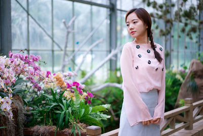 Thoughtful young woman standing by flowers in greenhouse