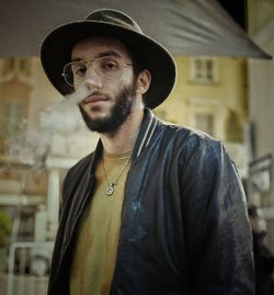 Low angle portrait of young man wearing hat standing against building