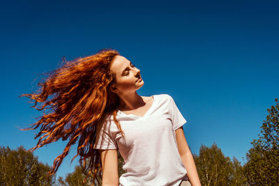 Low angle view of girl tossing hair against sky