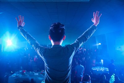 Rear view of young man with arms raised standing in music concert