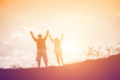 Low angle view of friends standing against sky during sunset