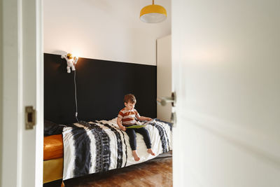 Boy reading book in bedroom seen through doorway