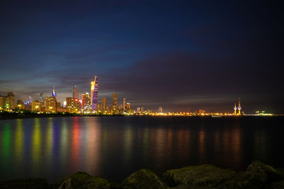 Illuminated buildings by sea against sky at night