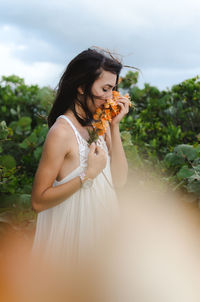 Young woman standing by flower tree against sky