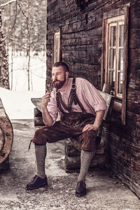 Full length of man with pipe sitting against house