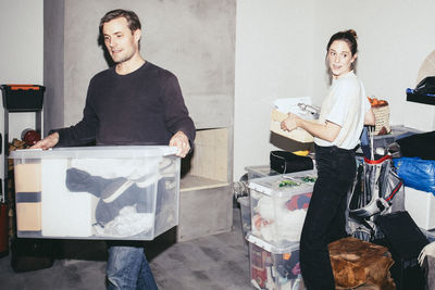 Man and woman helping each other while picking boxes during relocation of house