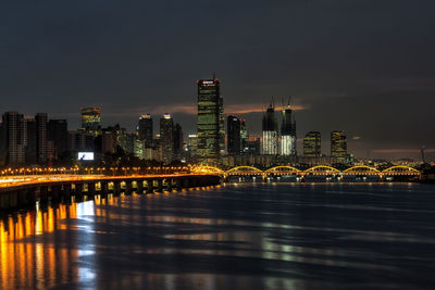 Illuminated city by river against sky at night