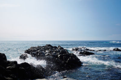 Sea waves splashing on rocks against sky