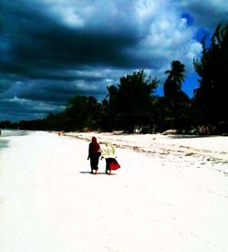 People on beach against cloudy sky