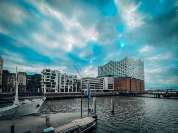 Buildings by river against cloudy sky