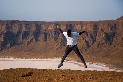 Rear view of man jumping on rock against sky