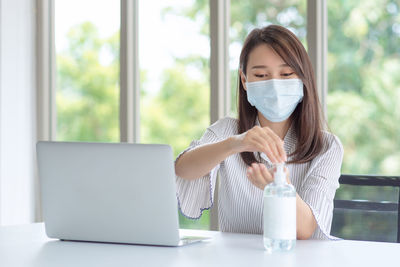 Young woman using sanitizer while sitting on table