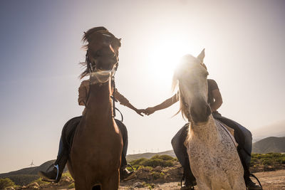 Couple riding horses on field against sky