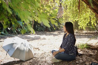 Woman sitting on field against trees