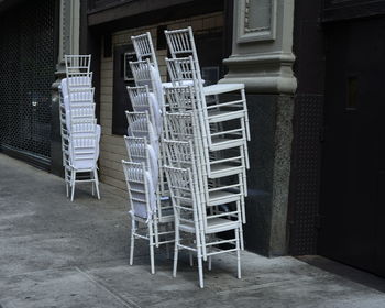 Stacked chairs on footpath against building