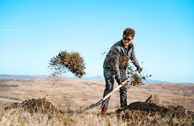 Man with shovel digging on field against clear sky