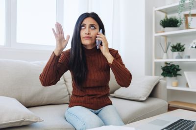 Young woman using mobile phone while sitting on sofa at home