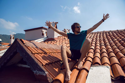 Man in the green t-shirt shorts and sunglasses sitting on the roof of a clay orange tile