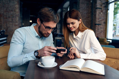 Young man and woman using phone in cafe