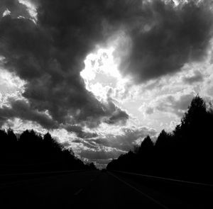 Road by silhouette trees against sky