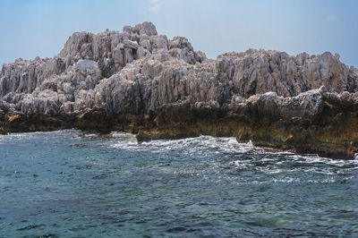 Rocky cliffs at seashore against sky