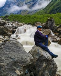 Side view of man sitting by stream in forest