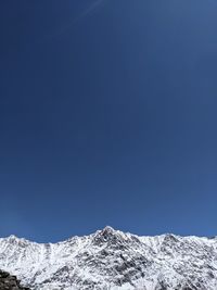 Low angle view of snowcapped mountains against clear blue sky