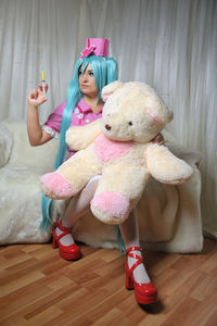 Young nurses with long blue hair injecting syringe to teddy bear at home