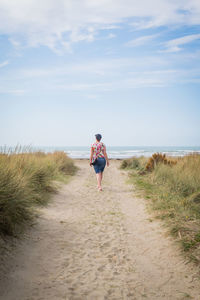 Rear view of woman walking at shore against cloudy sky