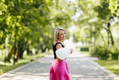 A young woman with cotton candy walks along an alley in the park.