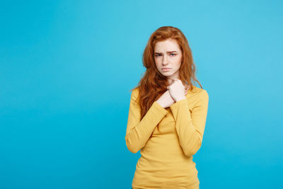 Portrait of worried young woman standing against blue background