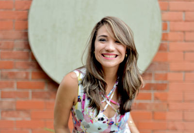 Portrait of a smiling young woman against brick wall