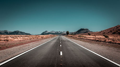 Road leading towards mountain against clear sky