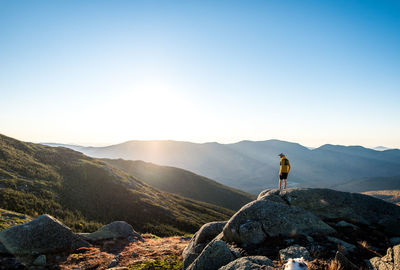 Man standing on rock looking at mountain against sky