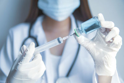 Midsection of doctor wearing mask holding syringe with medicine