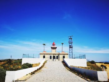 Lighthouse by building against blue sky