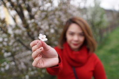 Woman with red knit holding a cherry blossom 