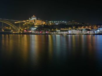 Illuminated city by river against sky at night