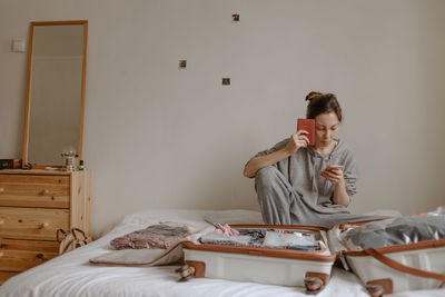 Woman checking list before going to airport, passport in her hand and open suitcase on the bed