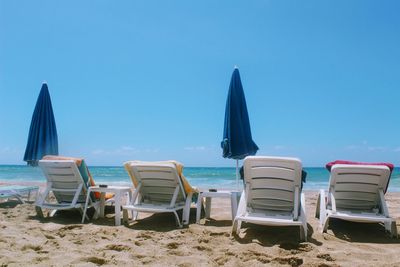 Chairs on beach against clear blue sky