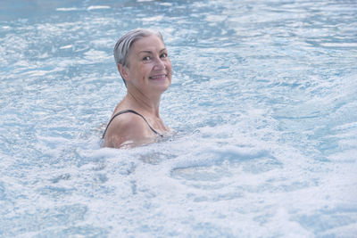 Senior caucasian woman with gray short wet hair enjoying in outdoor thermal swimming pool.